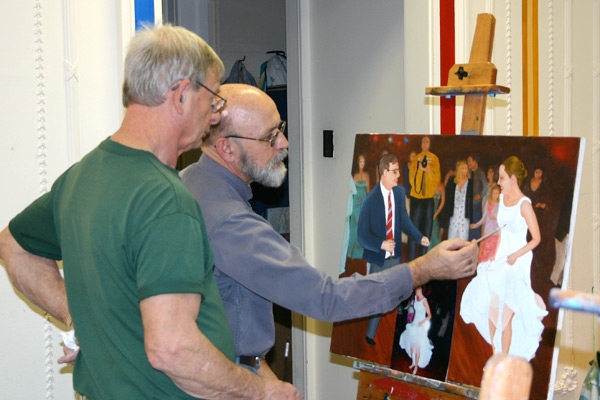 Two men look at a painting on an easel. The painting shows a man and woman danci